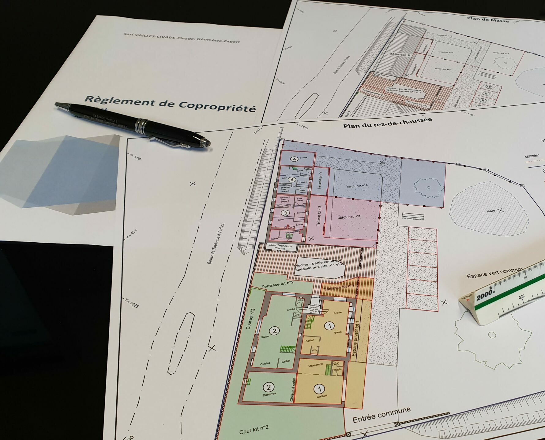 Plans de copropriété et document de règlement posés sur un bureau, accompagnés d’une règle de géomètre et d’un stylo.