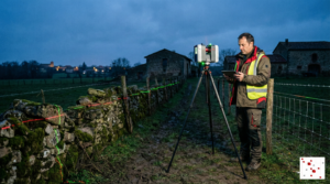 Géomètre expert utilisant un scanner laser 3D au crépuscule pour mesurer précisément une limite de propriété disputée (mur et clôture) entre deux terrains en Haute-Garonne.